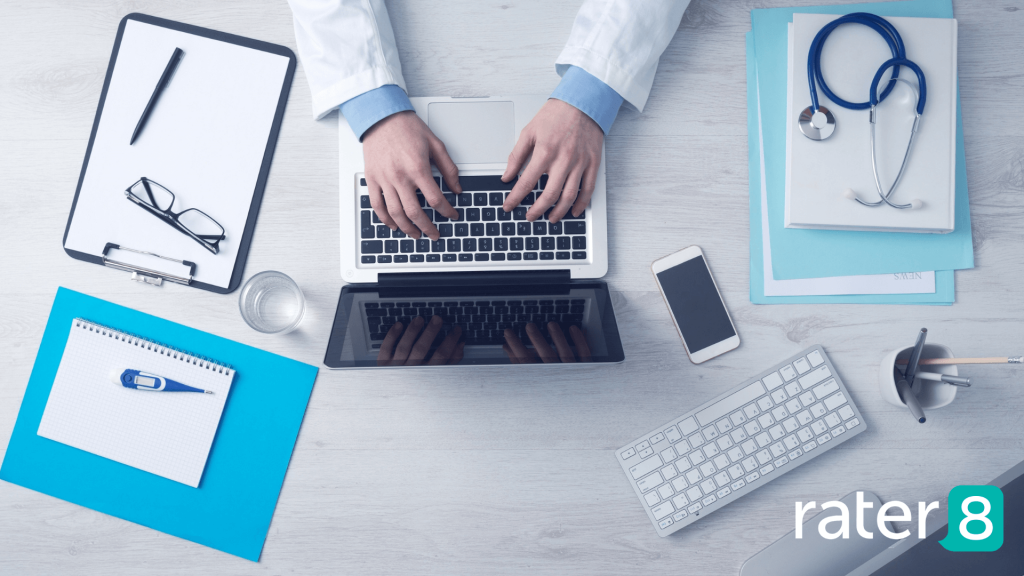 Overhead shot of doctor sitting at desk with laptop, notepad, clipboard, and stethoscope.