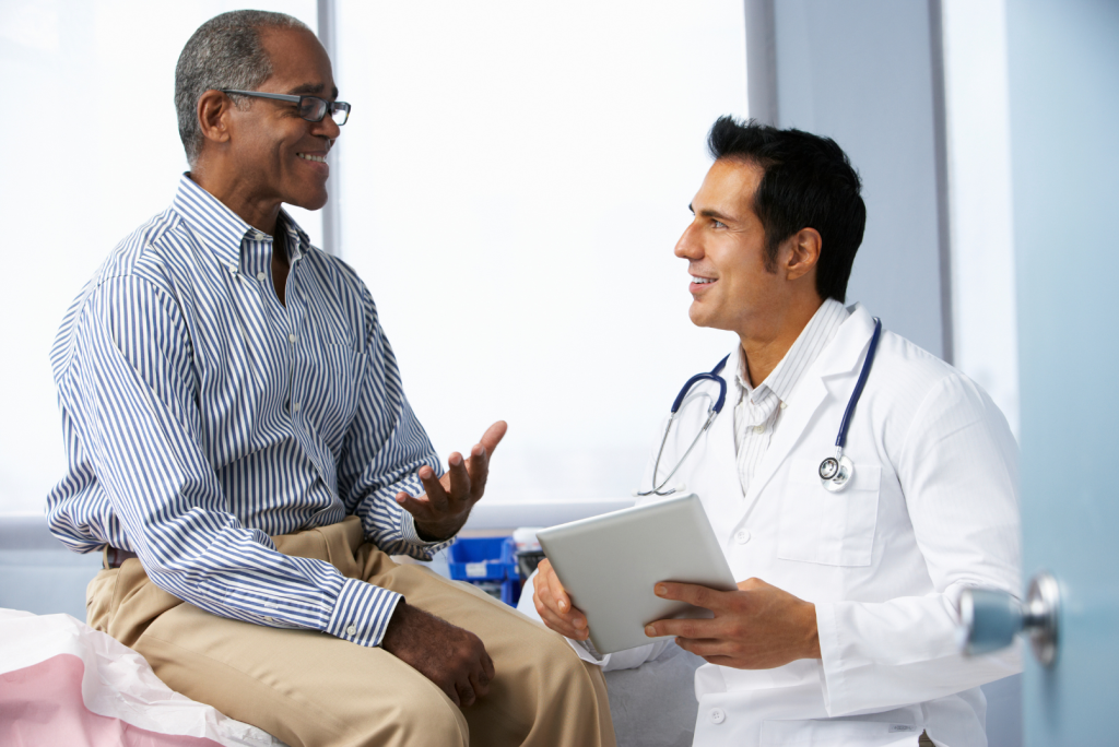 African American patient sits and talks with doctor, both smile.